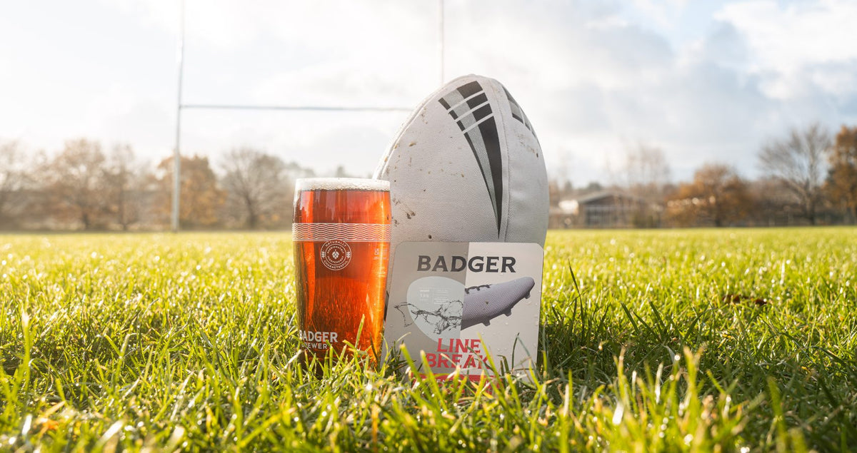 Pint of Badger beer beside a rugby ball on a pitch with goalposts behind