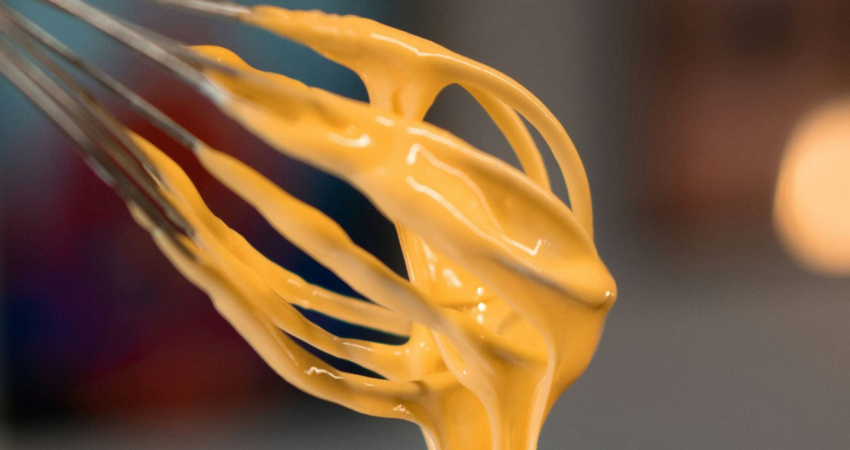 Beer cheese sauce dripping from a whisk in close-up