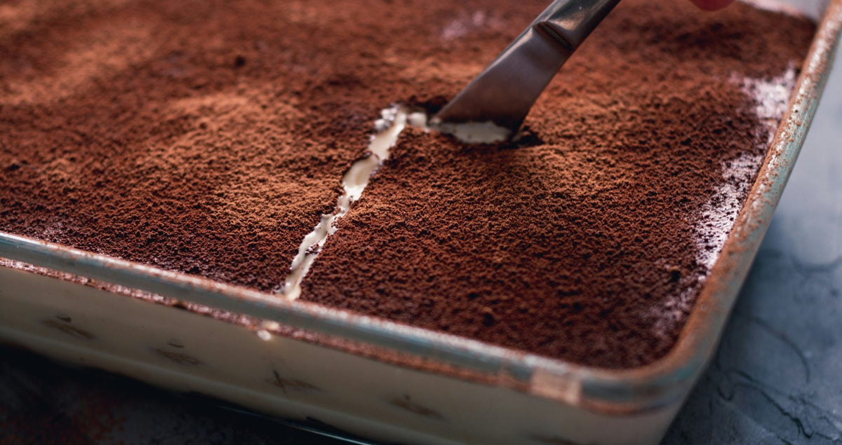 Beer tiramisu dusted with cocoa in a baking tin, with a spoon lifting a portion