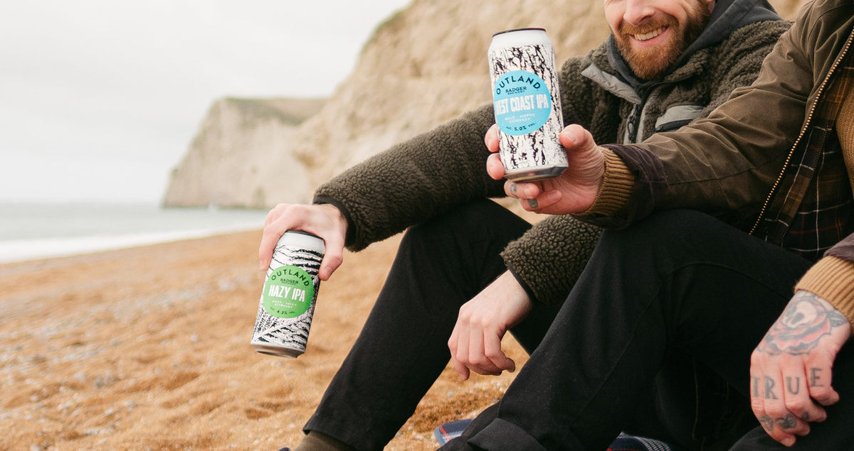 Two men on the beach holding cans from the Outland IPA range