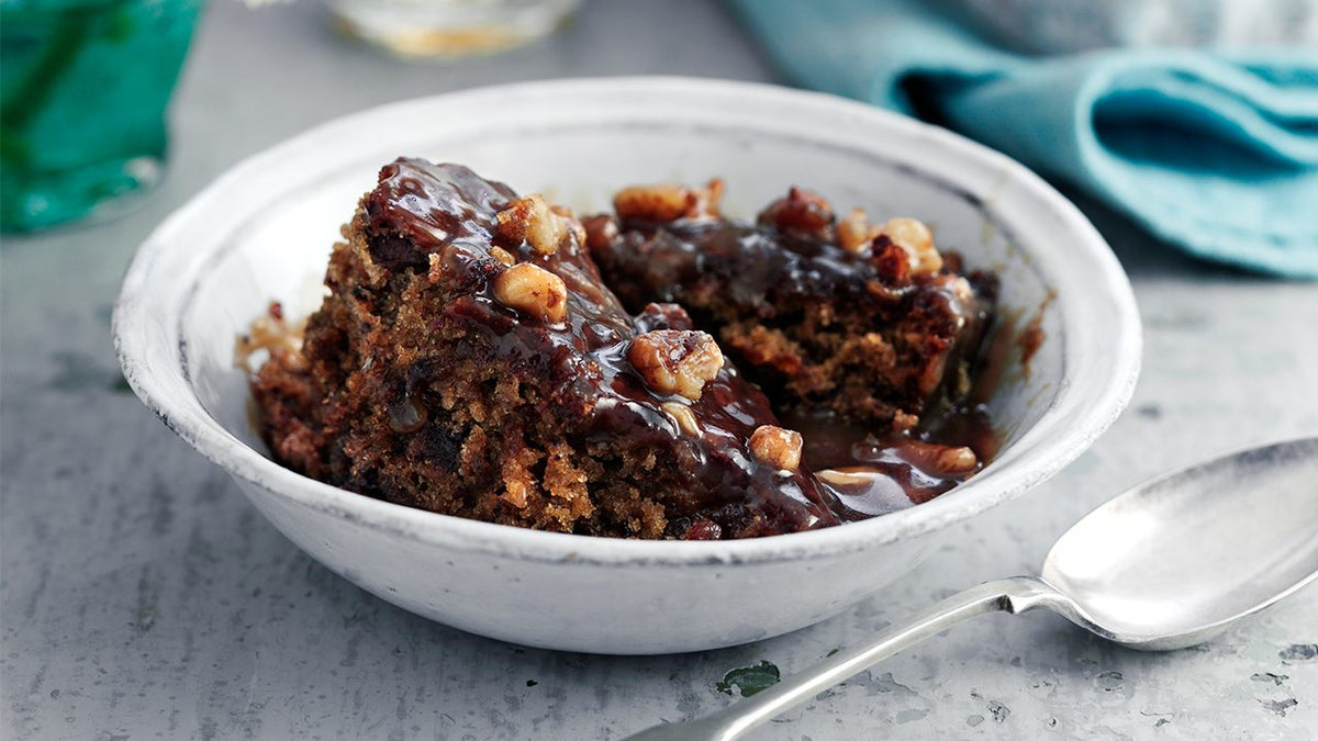 Sticky ginger and toffee pudding topped with walnuts in a white dish