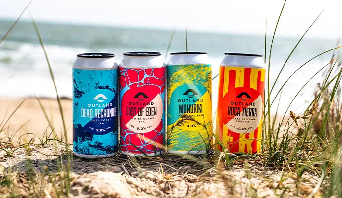 Four cans from the Outland range lined up in dune grass above a beach