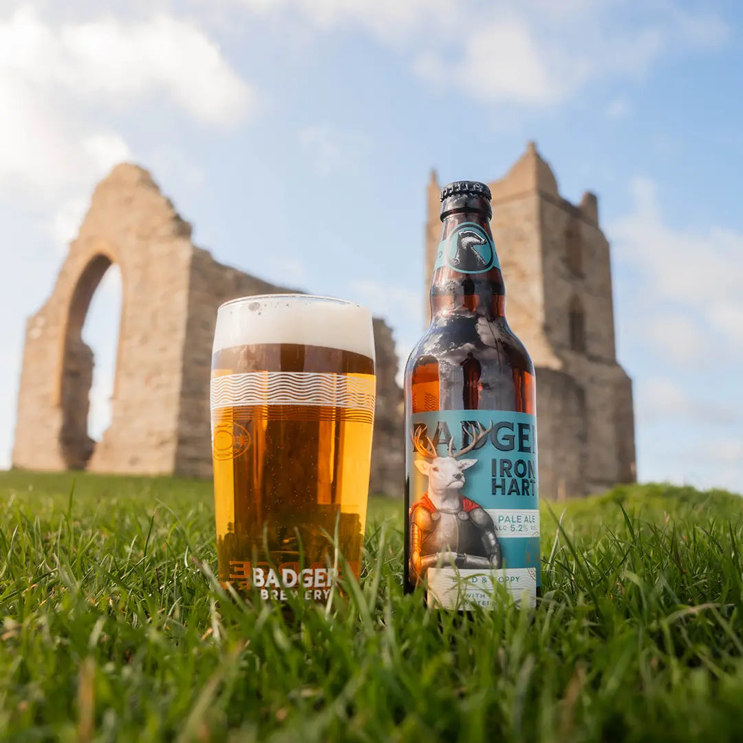 Bottle and full pint of Badger Iron Hart on grass in front of ruined stone arches