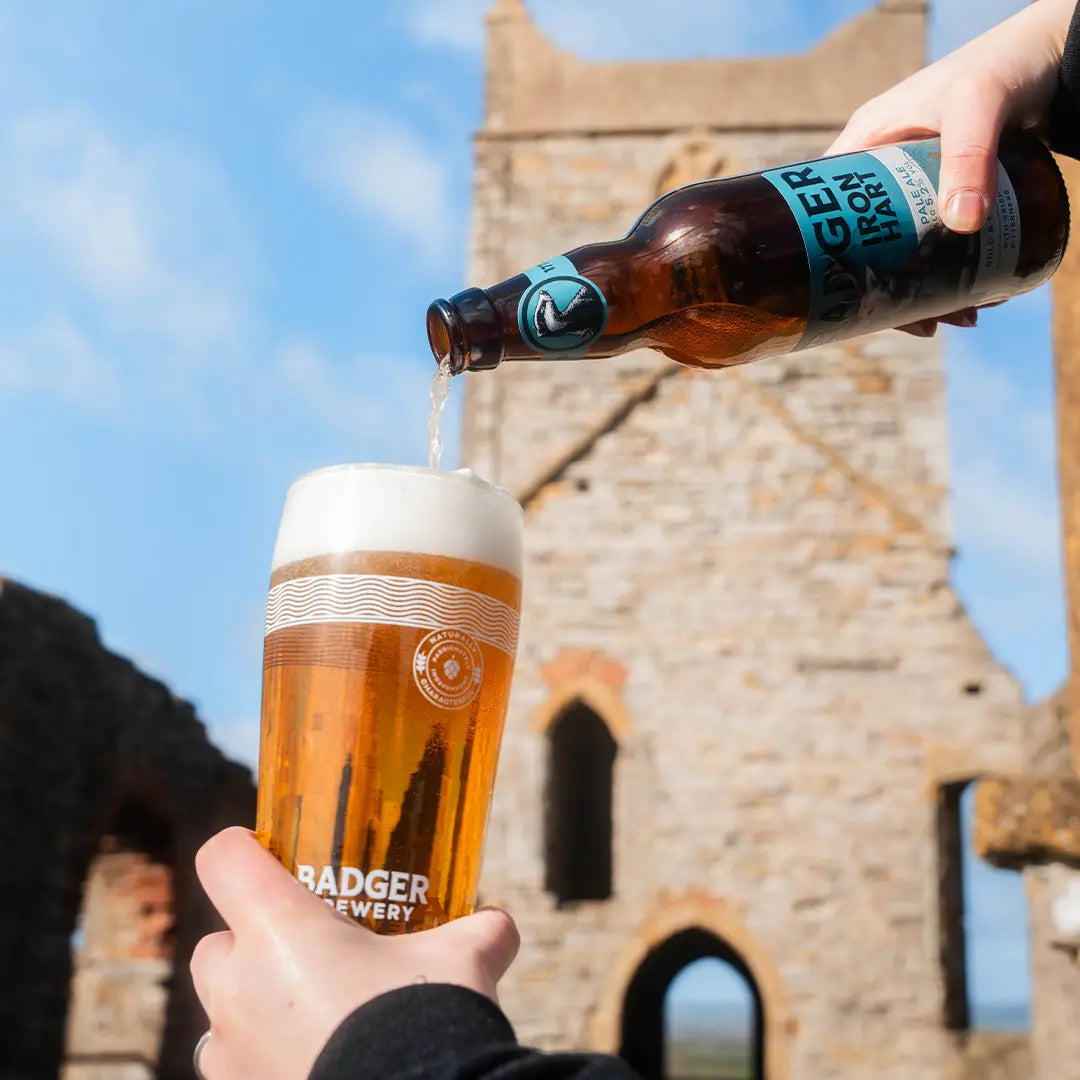 Badger Iron Hart poured from the bottle into a branded glass inside a stone castle ruin