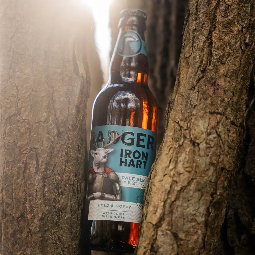 Bottle of Badger Iron Hart pale ale propped against the trunk of a tree