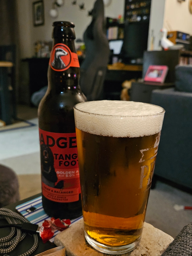 A bottle of Badger Tangle Foot golden ale beer and a frothy glass of the beer in a home setting.