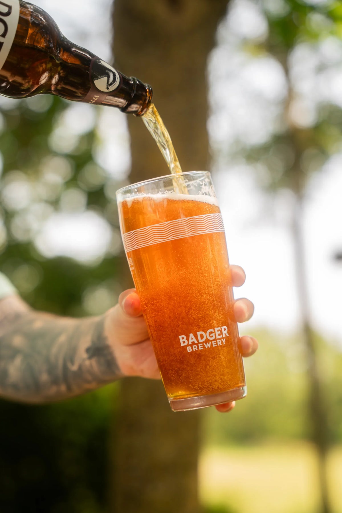 Kindness IPA poured into a glass held outdoors in front of a green field