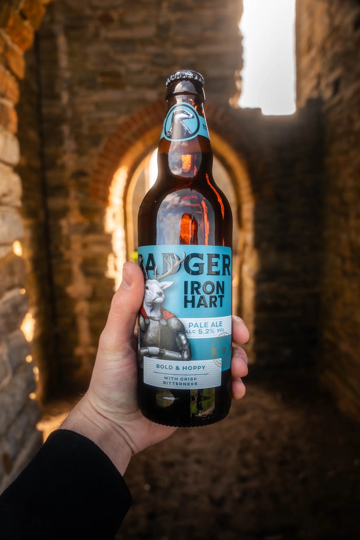 Bottle of Badger Iron Hart held up in the window of a castle ruin