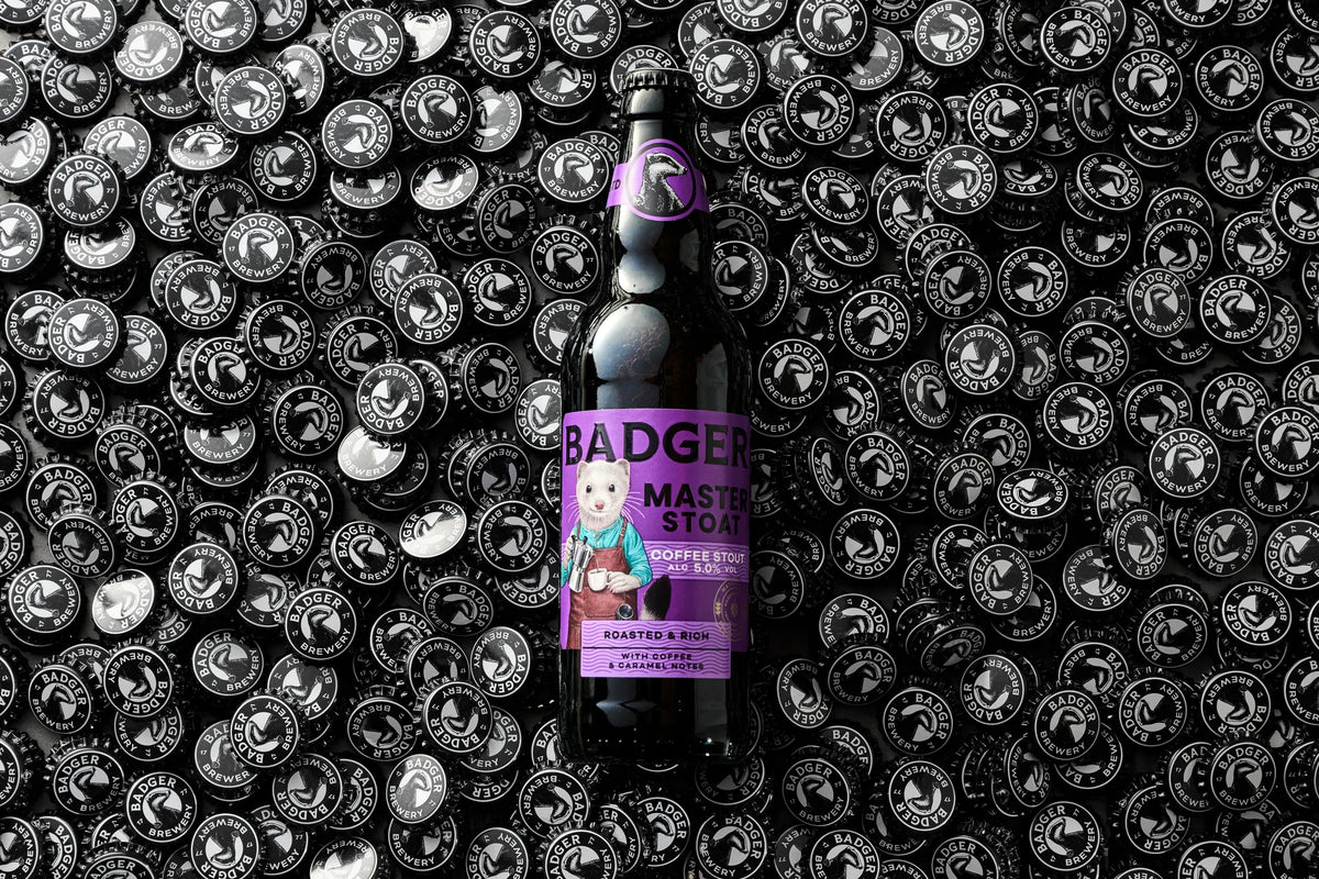Bottle of Badger Master Stoat laid flat on a bed of black and white bottle caps