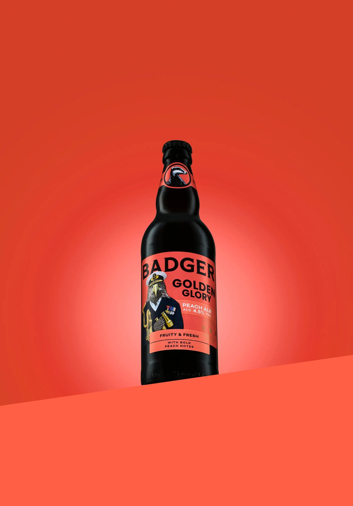 Bottle of Badger Golden Glory peach ale on a coral red background