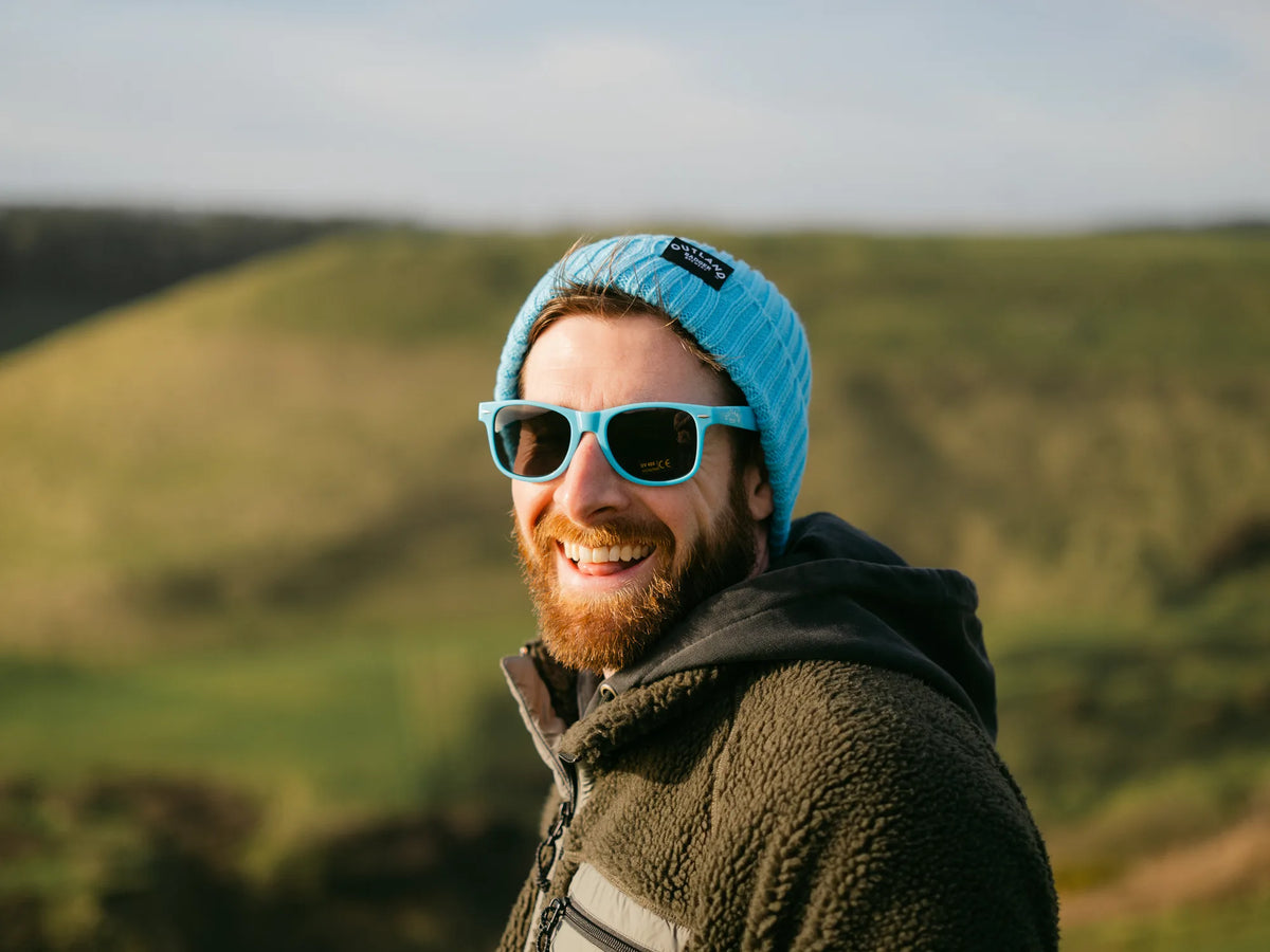 Man wearing a turquoise Outland beanie and blue Outland sunglasses outdoors