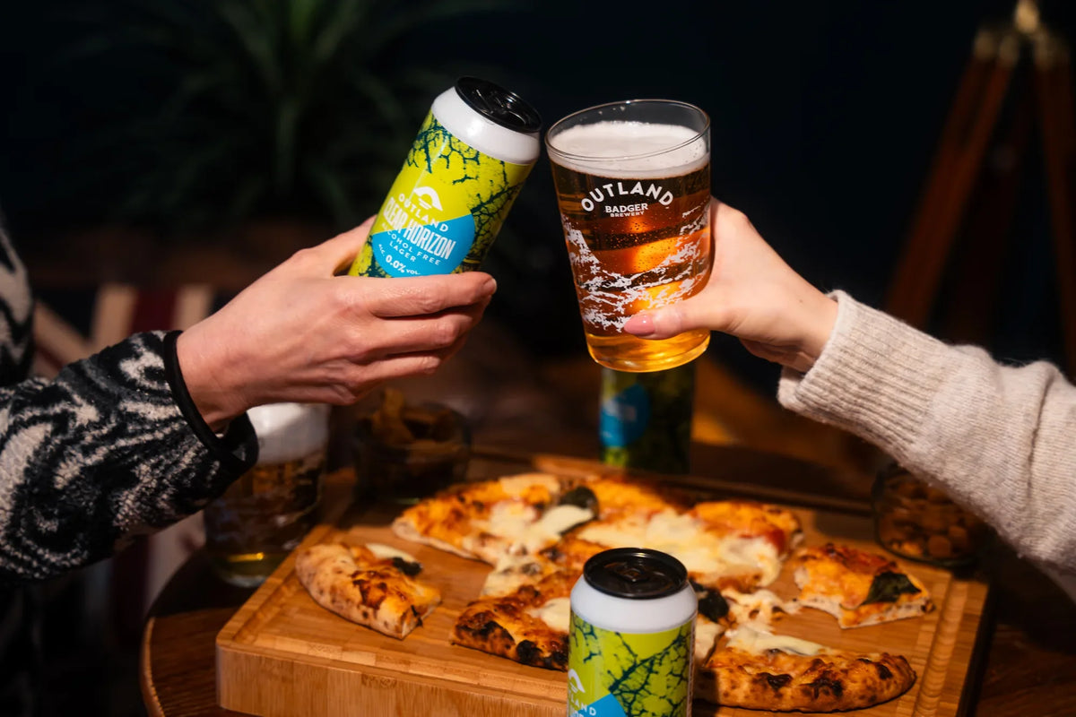 Two Outland pints raised over a sharing pizza board with cans of Clear Horizon on the table