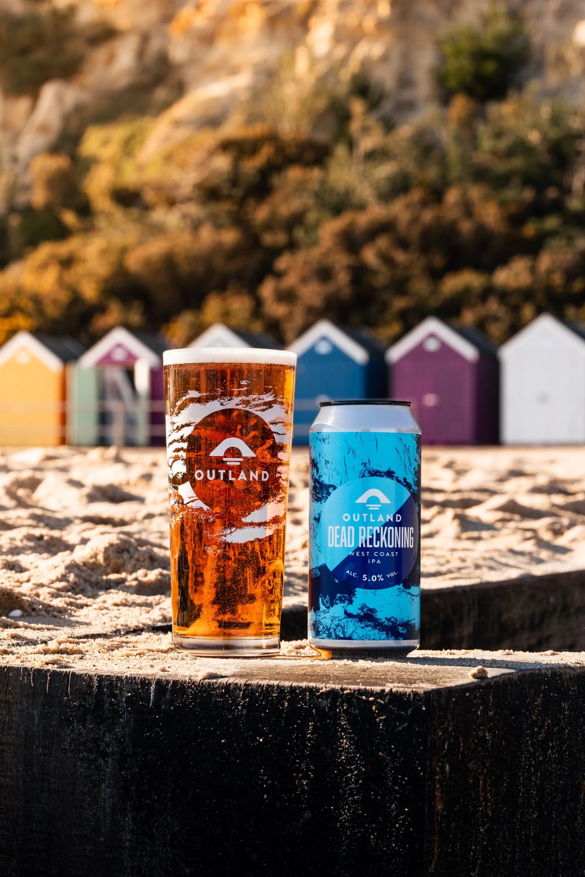 Two Outland pints and a can of Dead Reckoning on a post in front of beach huts
