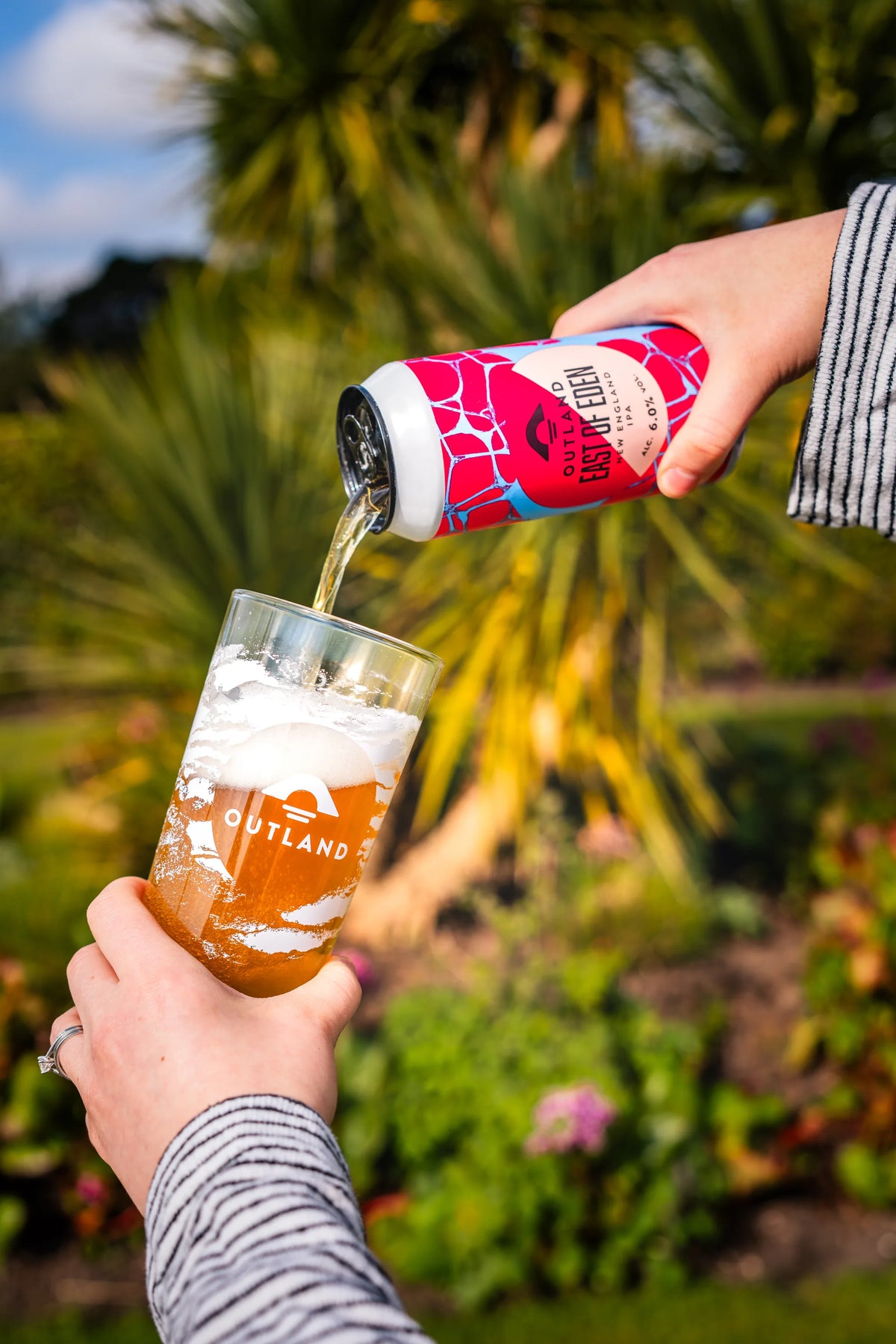 Can of Outland East of Eden poured into a glass in a tropical planted garden