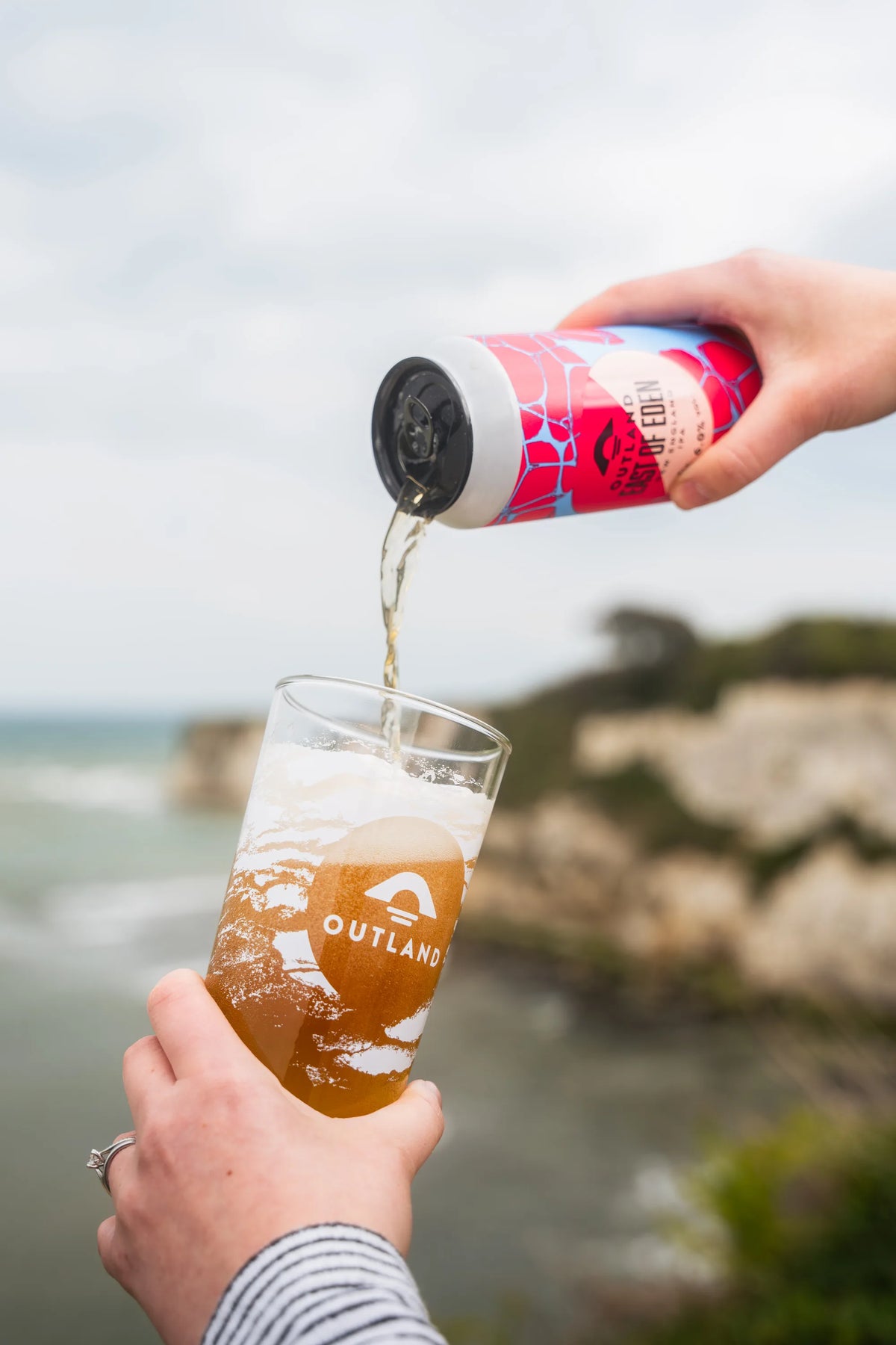 Can of Outland East of Eden poured into a glass held above a rocky coastline