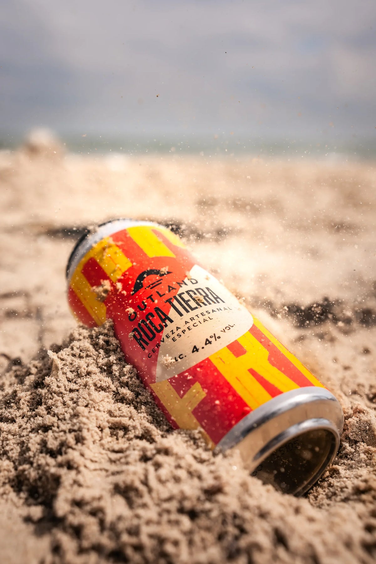 Can of Outland Roca Tierra lying on rippled beach sand