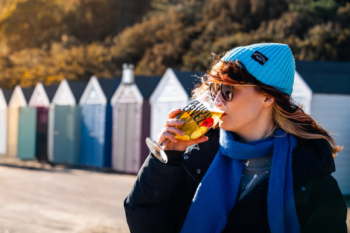 Two photos side by side of people in Outland beanies drinking beer at beach huts and on a hillside