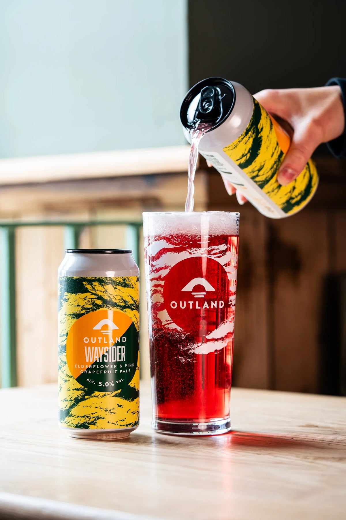 Outland Waysider poured into a glass on a pub table beside two cans