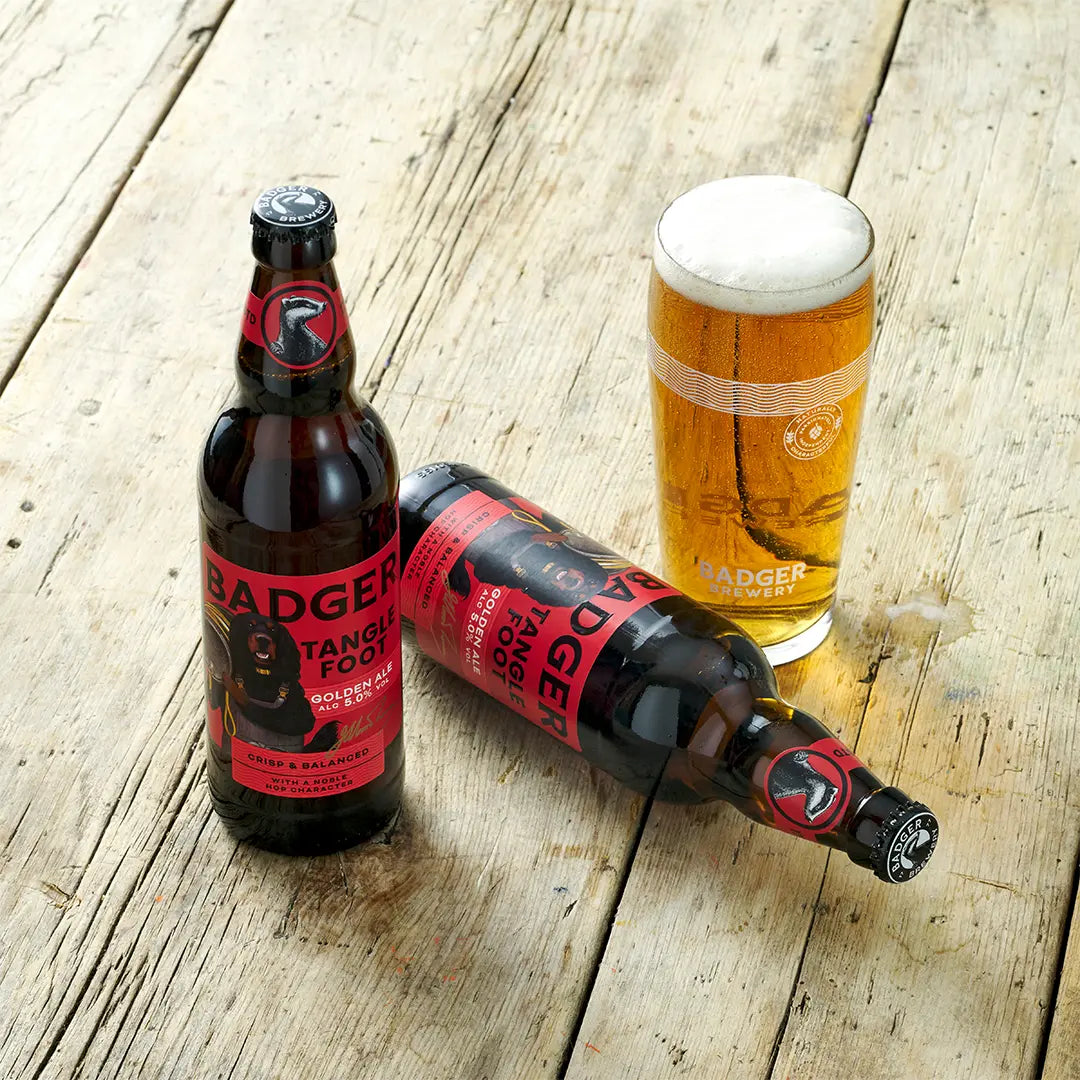 Two bottles of Badger Tangle Foot and a full pint glass on weathered wooden decking
