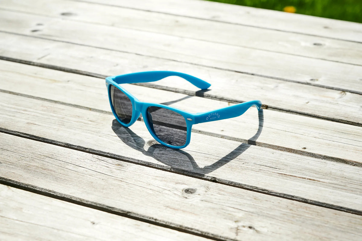 Blue Outland sunglasses folded on a weathered wooden picnic table