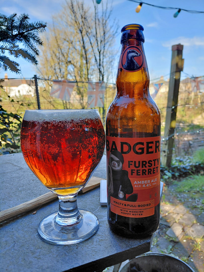 Bottle and stemmed glass of Badger Fursty Ferret on a table with festoon lights