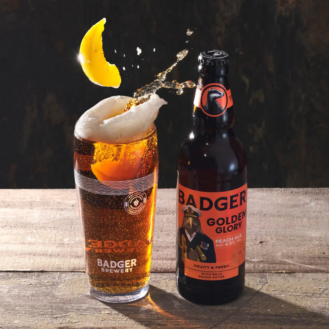 Badger Golden Glory poured into a glass with a peach slice garnish on a wooden table