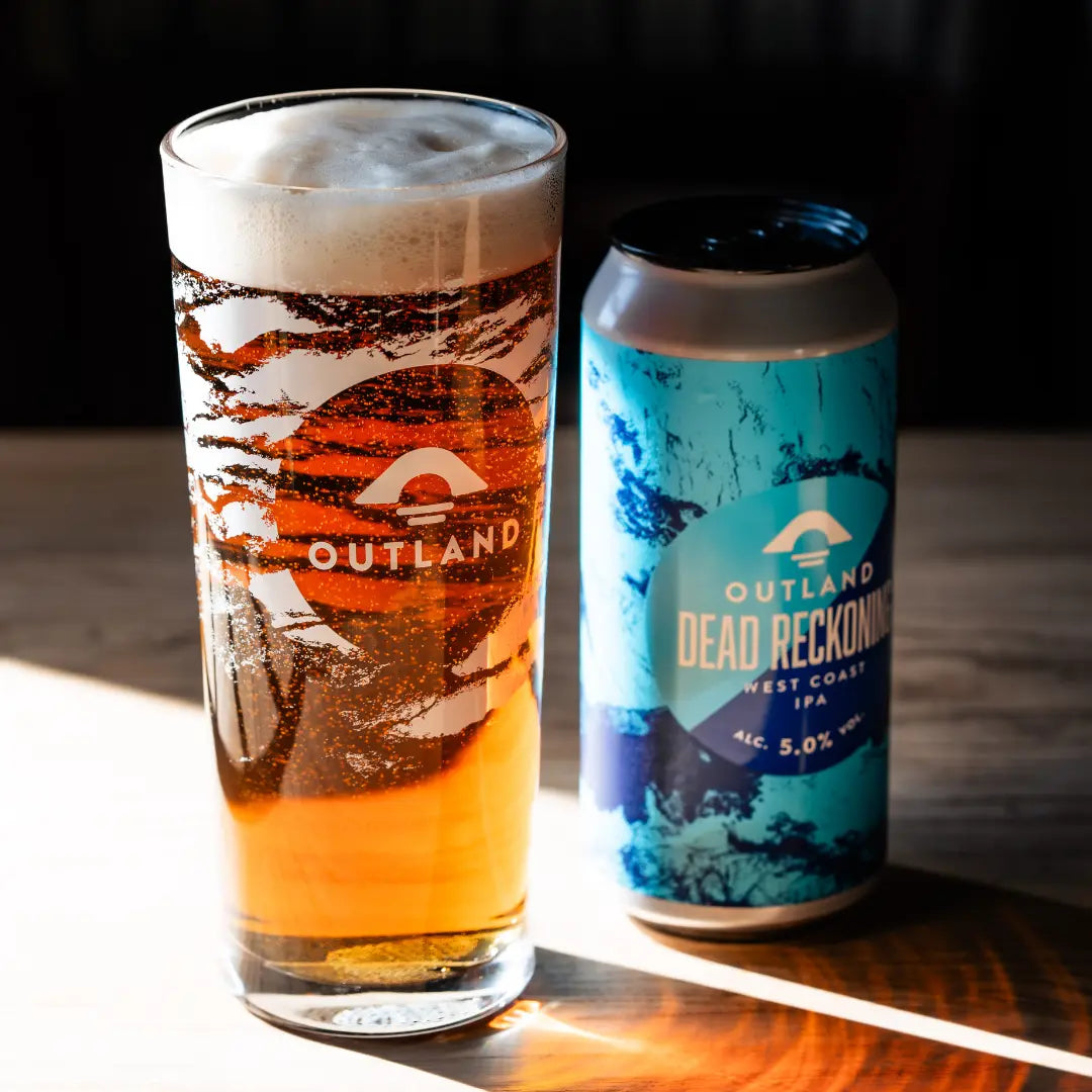 Pint glass of Outland Dead Reckoning IPA beside its can on a wooden table