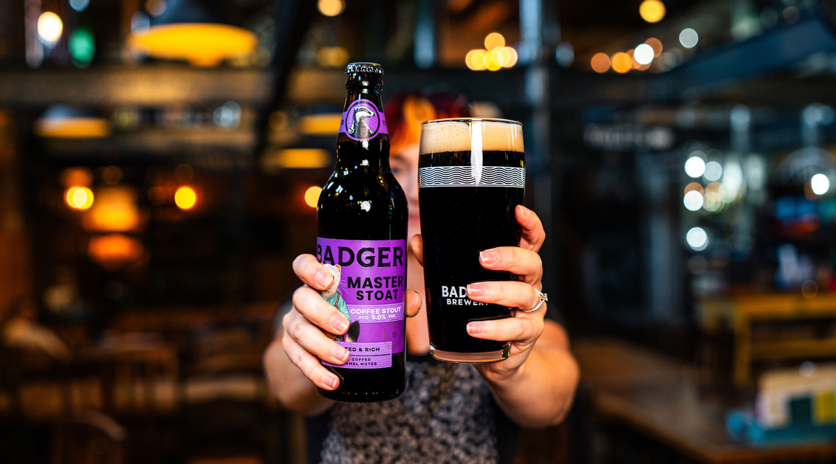 Person holding bottle and pint of Badger Master Stoat in pub