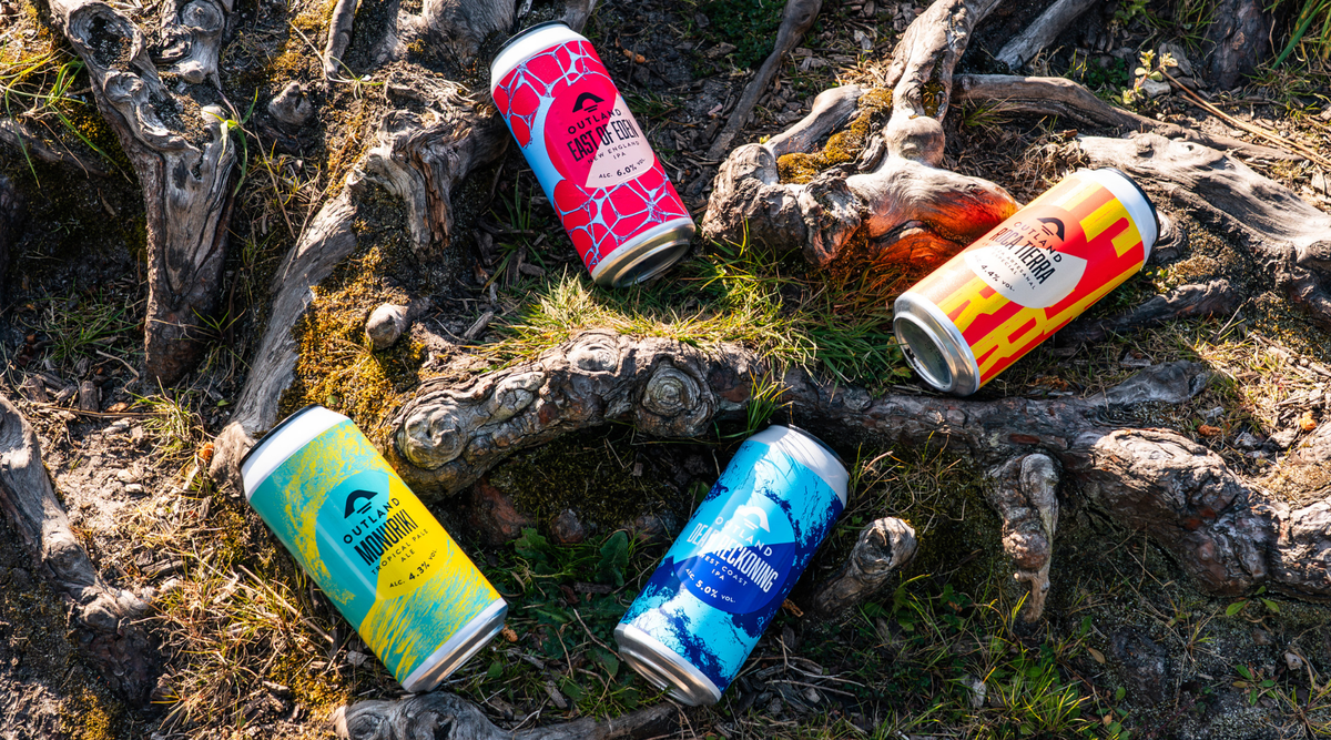 Cans of Outland craft beer laid out on mossy tree roots in woodland