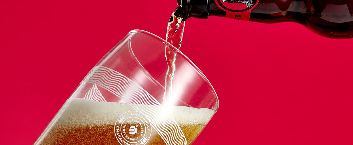 Badger ale poured into a branded glass on a deep pink background