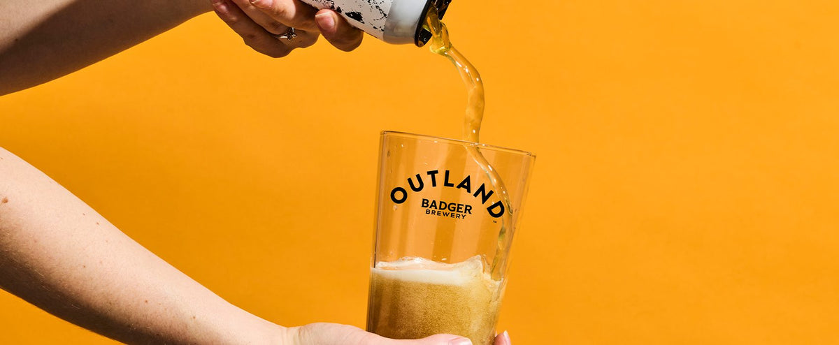Badger pale ale poured into an Outland branded glass on a yellow background
