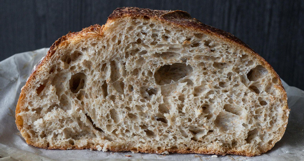 Cut loaf of freshly baked beer bread showing an open crumb, on a dark board