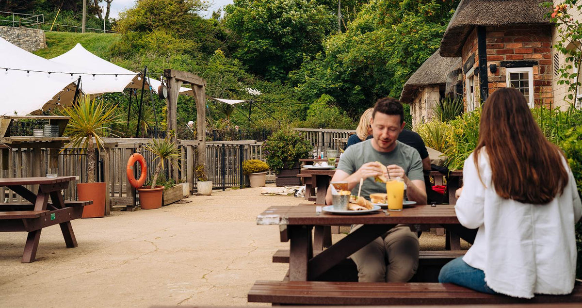 Couple eating and drinking at a picnic bench in a Hall & Woodhouse beer garden
