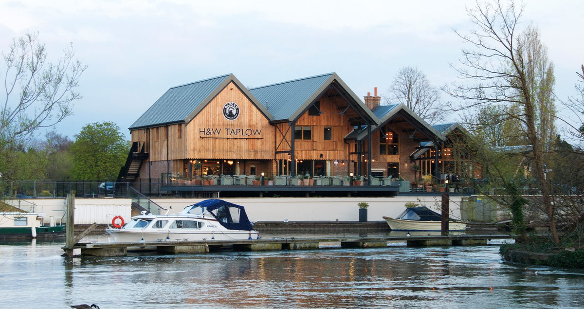 Hall & Woodhouse riverside pub with moored boats on the water in front of it