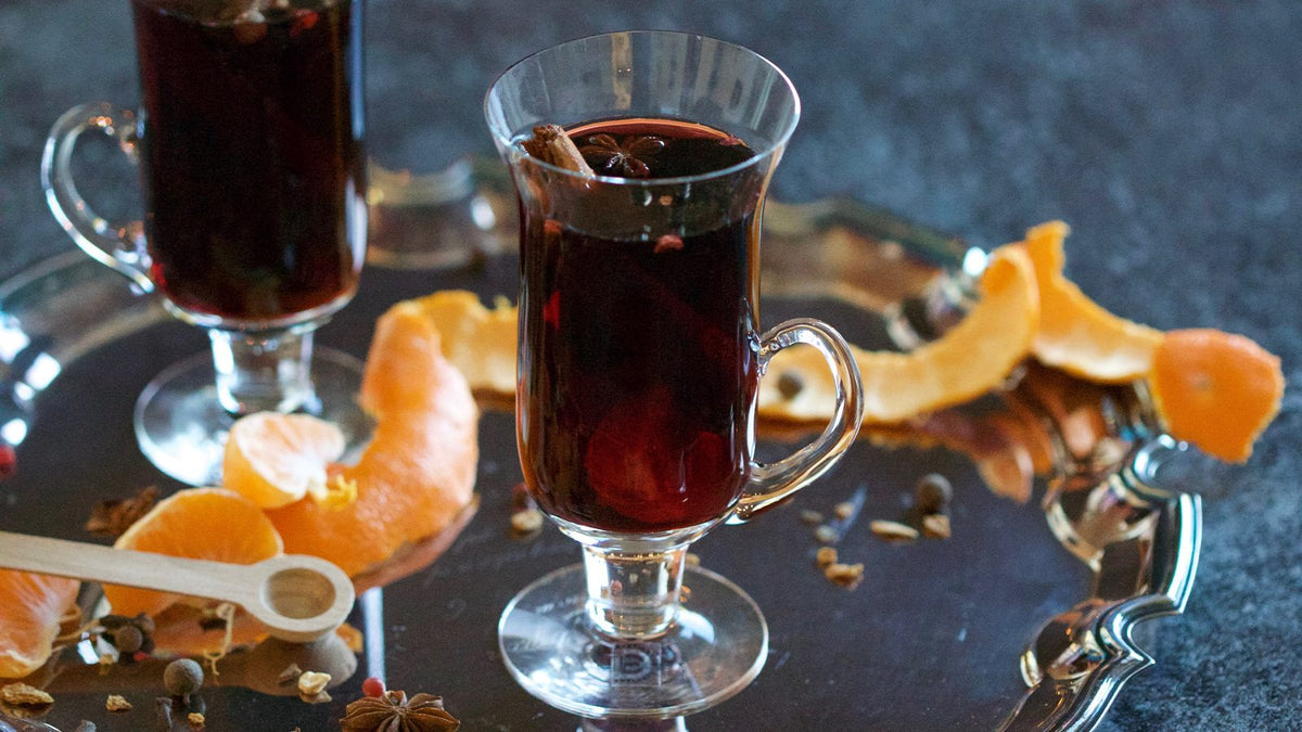 Two glass mugs of mulled spiced beer with orange peel garnish