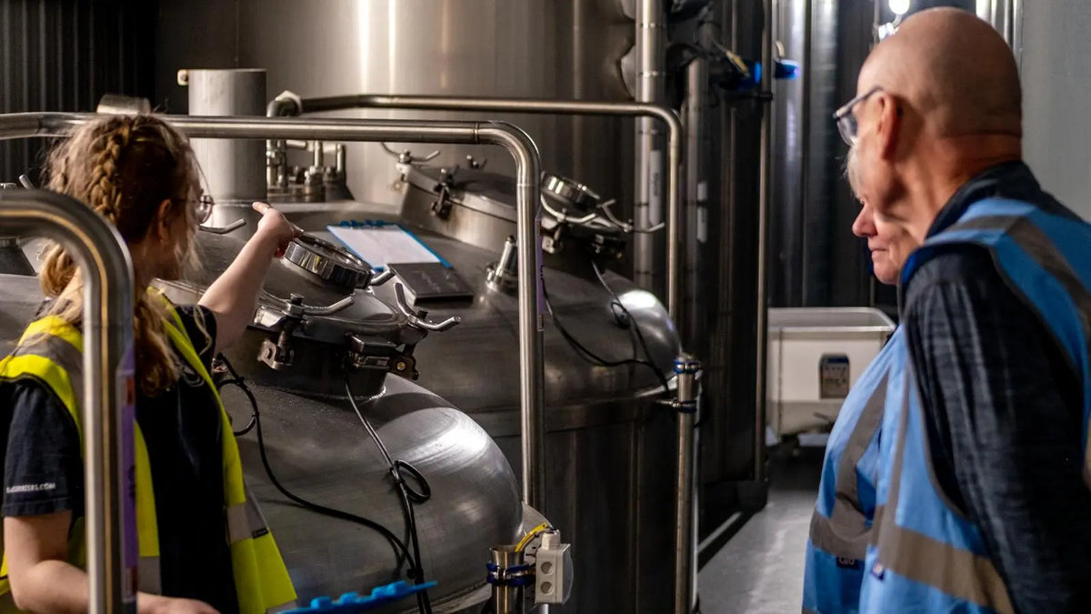 Brewer in high-visibility overalls working beside stainless steel fermentation tanks