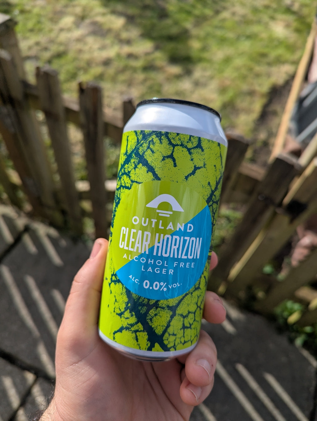 Hand holding a can of Outland Clear Horizon alcohol-free lager in a garden