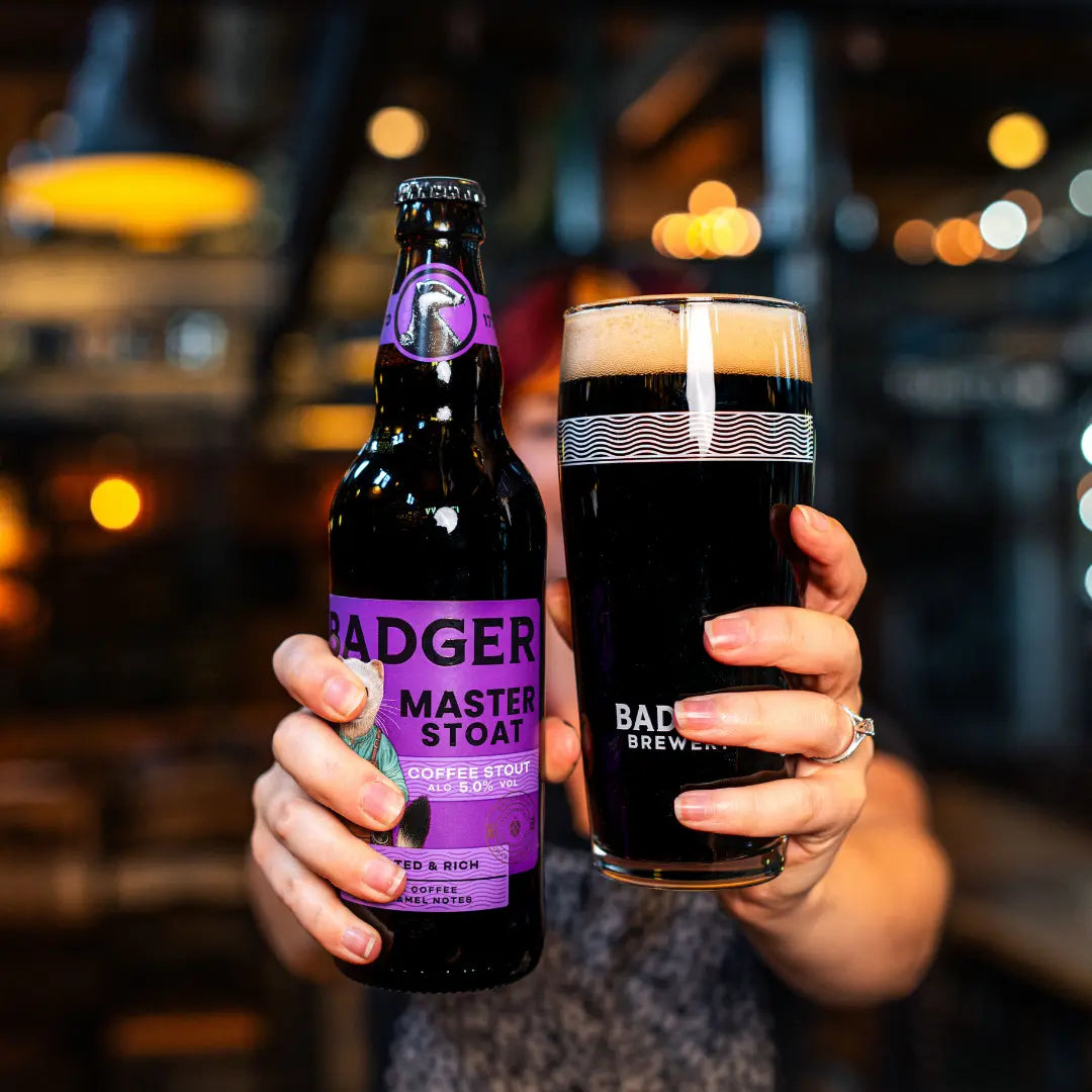 Two people holding a bottle of Badger Master Stoat and a dark pint in a bar
