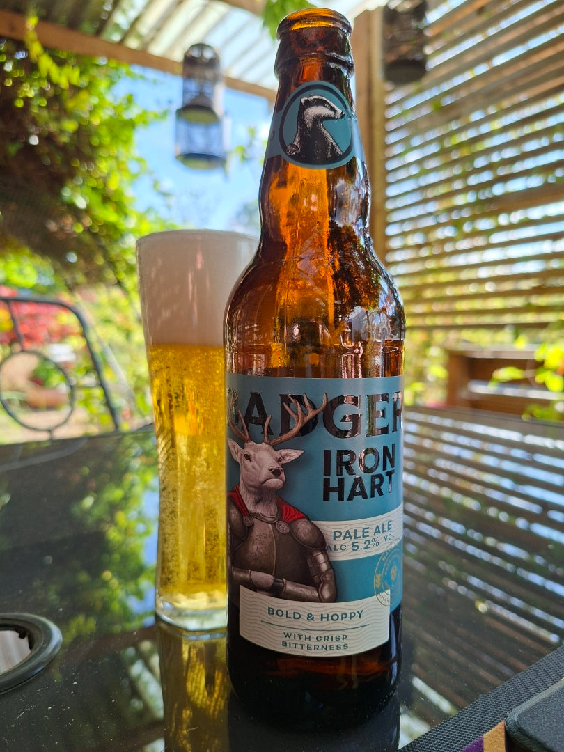 Bottle of Badger Iron Hart and a full glass on a table under a pergola