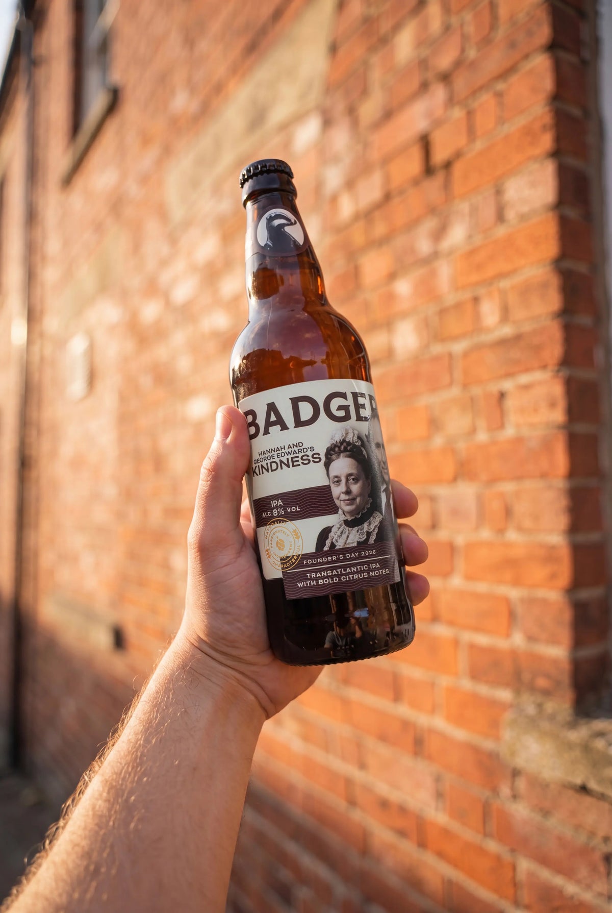 Hand holding a bottle of Badger Founder's Day ale against a brick wall