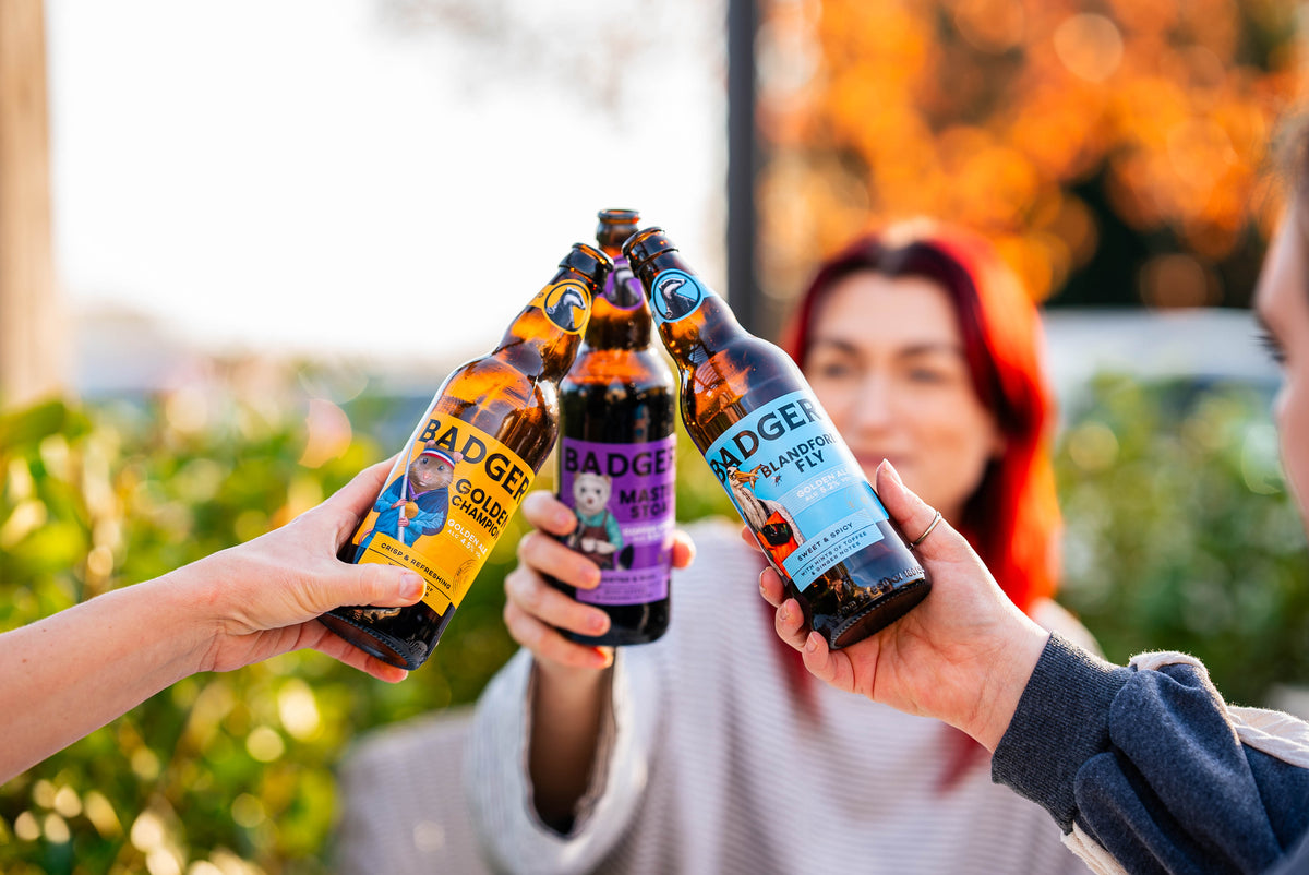 Two people toasting with a fan of Badger and Outland bottles outdoors in autumn