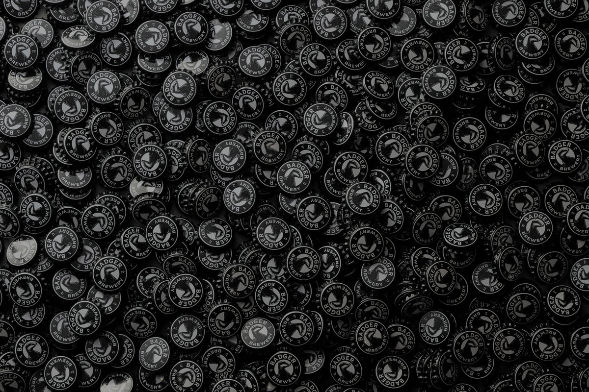 A dense pile of round black Badger Brewery bottle crowns with white printed text and a central emblem