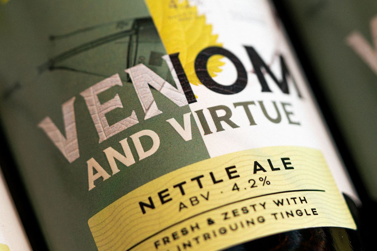 Close-up of a Venom and Virtue Nettle Ale bottle label, showing dark green, white, and pale yellow packaging with bold lettering.