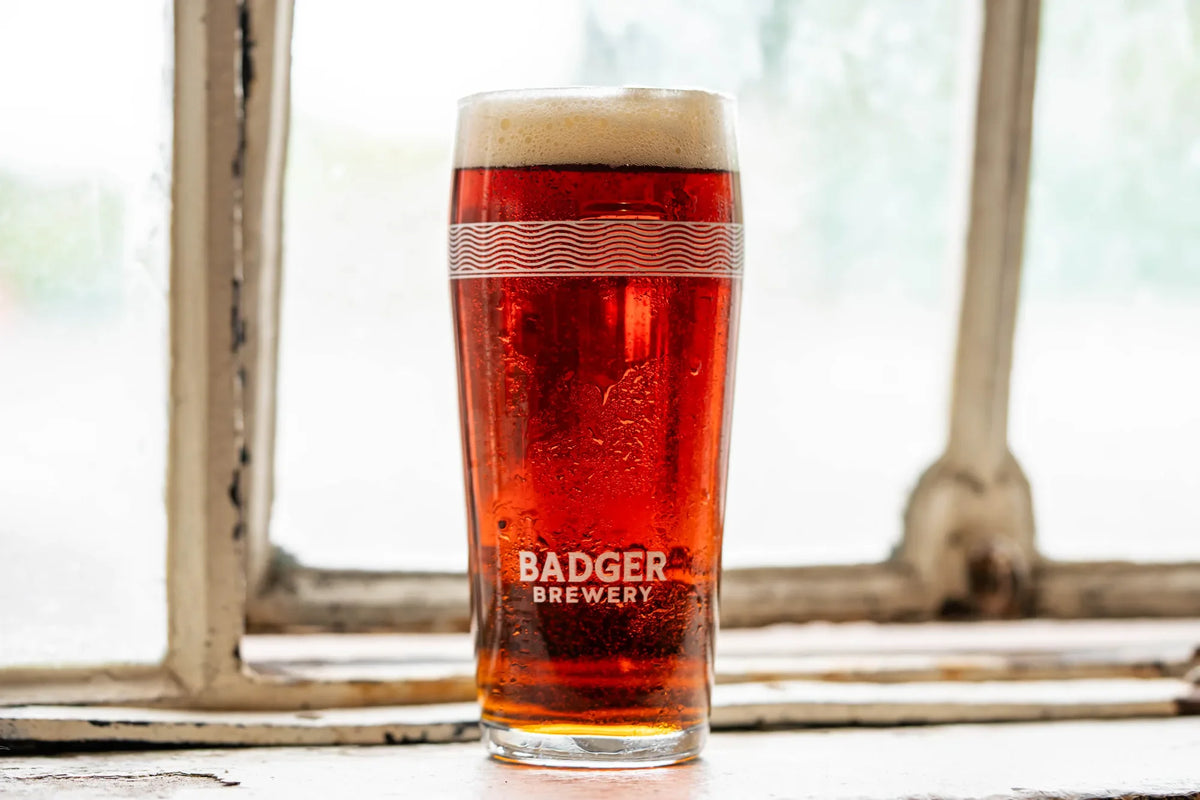Badger pint glass of Cranborne Poacher ruby ale on a sunlit stone window ledge