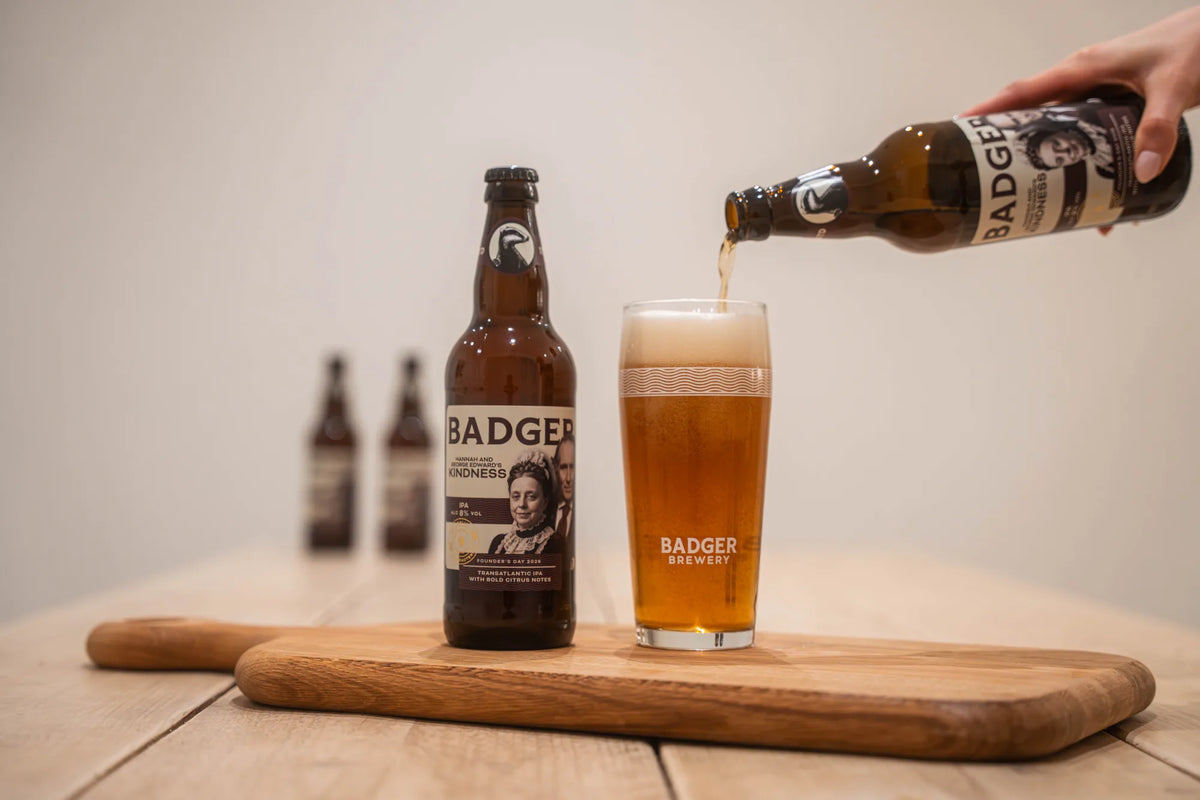 Bottles and a full glass of Badger Kindness IPA on a wooden serving board