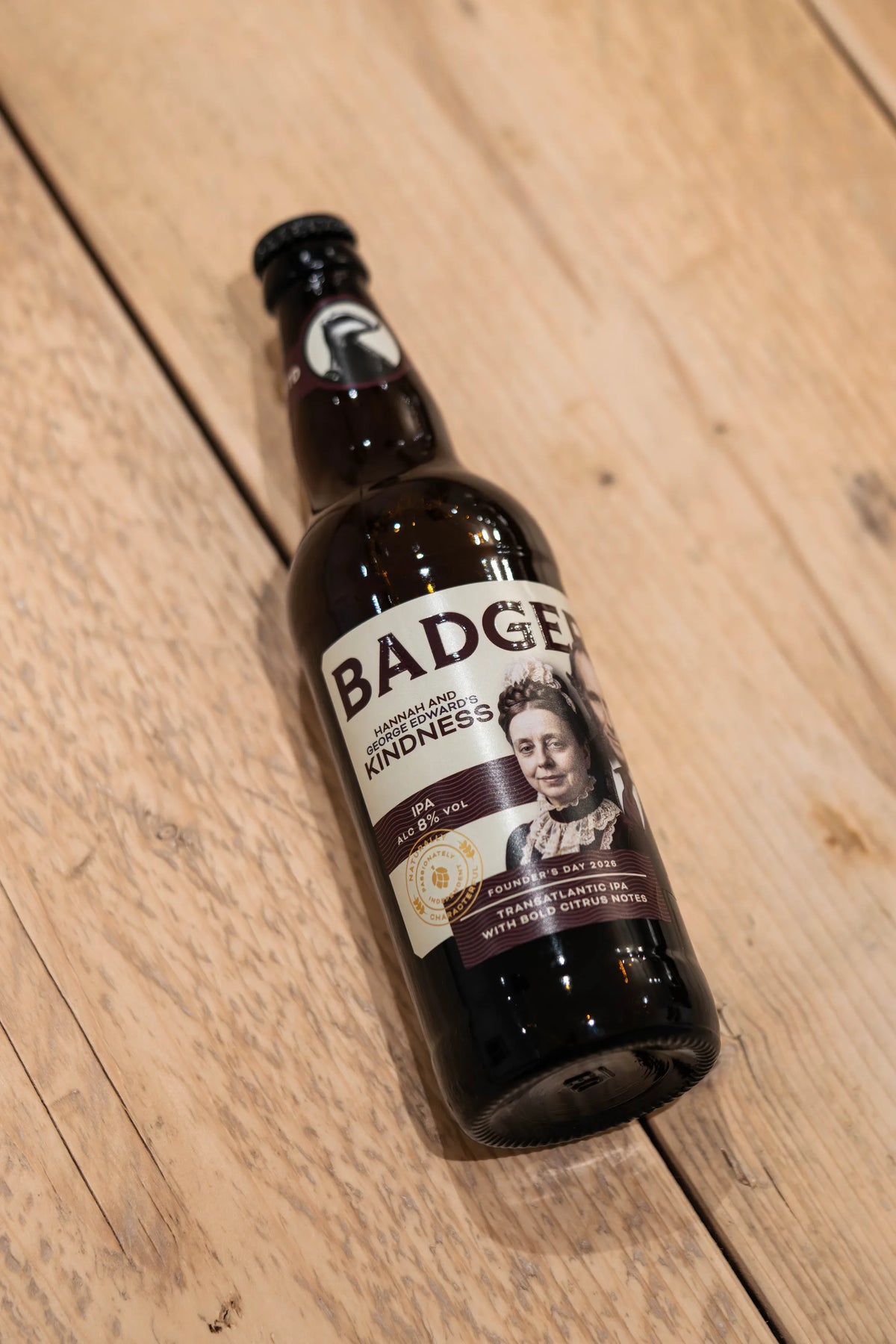 Bottle of Badger Kindness IPA lying on pale wooden decking