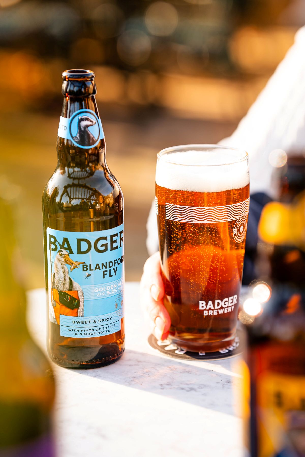 Bottle of Badger Blandford Fly beside a full pint glass on a beer garden table