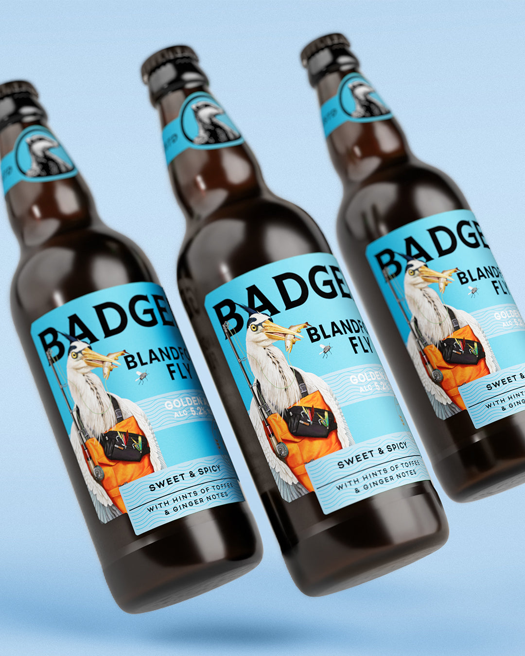 Three dark brown glass beer bottles of Badger Blandford Fly with blue labels featuring a pelican illustration and the brand name BADGER, shown on a light blue gradient background.