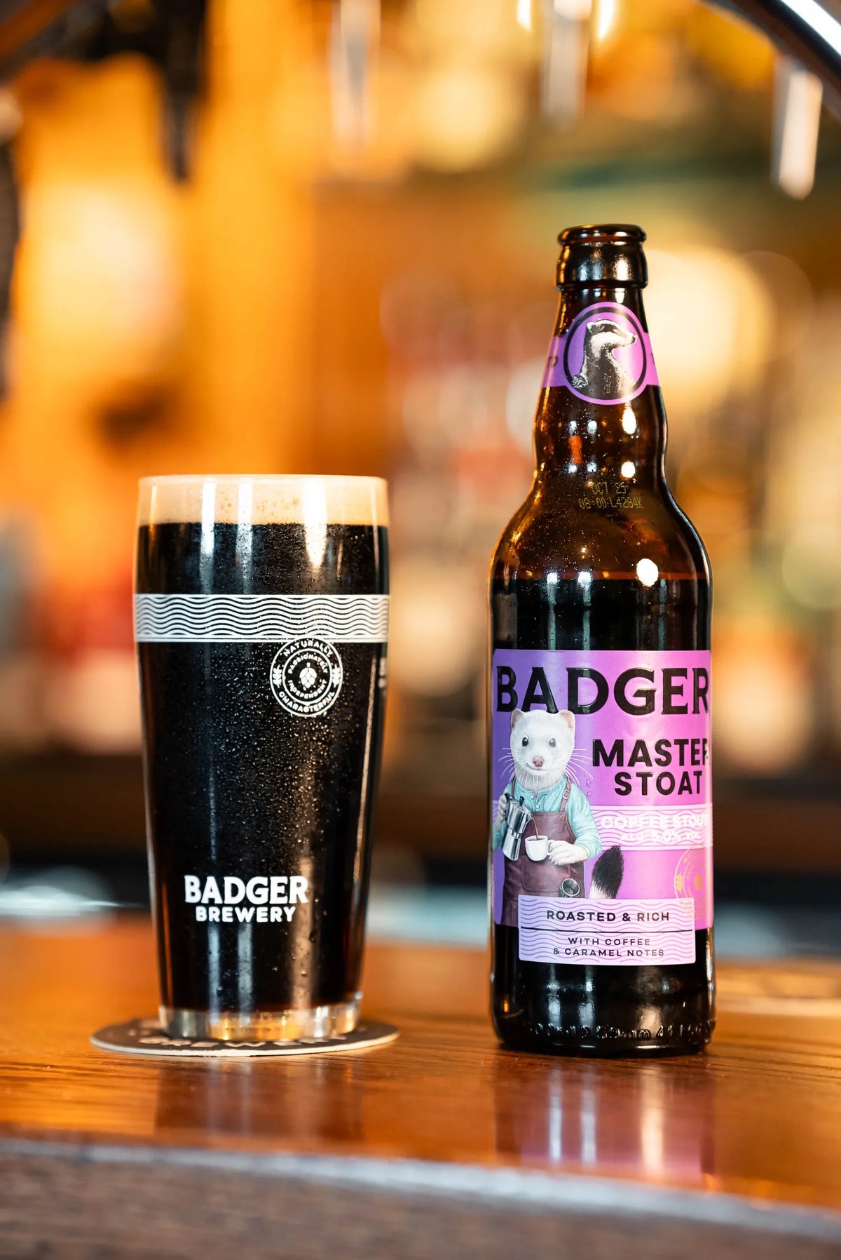 Bottle of Badger Master Stoat beside a full dark pint on a pub bar