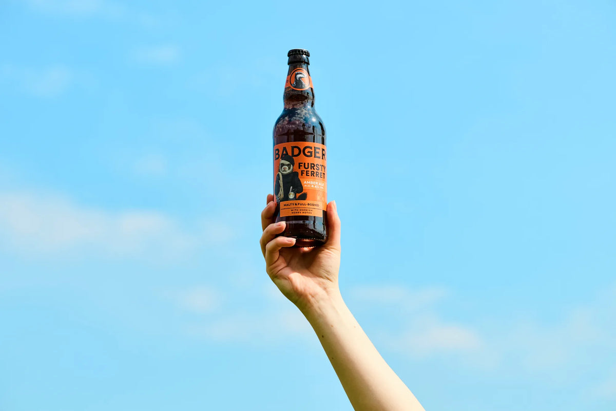 Hand holding a bottle of Badger Fursty Ferret up against a bright blue sky